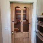 French doors with arched glass panes and solid lower panels, raw wood finish, installed in cased opening.