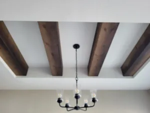 Dark stained parallel wood ceiling beams with a black chandelier hanging between them