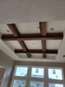 Dark stained boxed ceiling beams forming a grid below a textured upper ceiling with windows