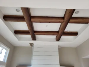 Dark stained boxed ceiling beams forming a grid above a shiplap clad stairwell wall