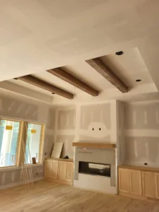 Painted wood ceiling beams over an unfinished room with a fireplace and bare oak flooring