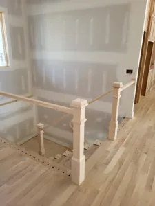 Unfinished wood newel posts and handrail framing a stairwell opening in hardwood flooring