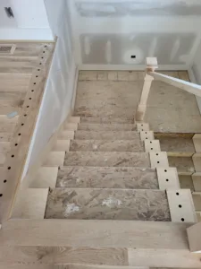 Stairs under construction, OSB treads with a drilled baluster stringer and a newel post test fit at the top.