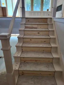 Unfinished stair treads with curved wood end caps and drilled holes for balusters