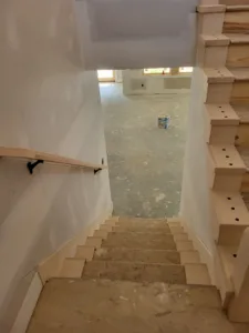Unfinished stair treads with curved wood end caps viewed down an open stairwell