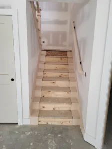 Interior stair with tread covers over pine risers, small end caps beside each tread and a wall handrail on black brackets