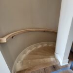 Curved staircase with finished treads, painted risers, and handrail installation in progress.