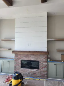 White shiplap accent wall installed above fireplace with wood mantel and brick surround during construction.