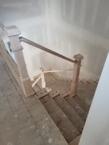 Wood newel posts and handrail installed at a stair landing with drilled baluster holes