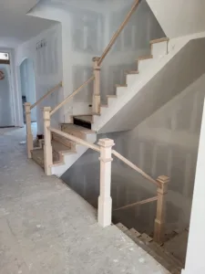 Staircase with raw wood treads and unfinished newel posts and handrail, drywall stage