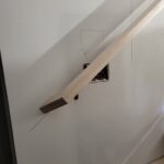 Handrail installation in progress on stairwell wall with brackets and mounting hardware visible.