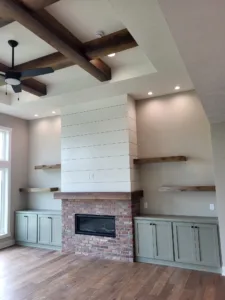 Finished built-in cabinetry and floating shelves flank a shiplap fireplace wall under beamed ceiling