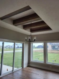 Dark stained wood beams forming a coffered tray ceiling above a chandelier and patio doors