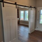 Completed barn doors with black track hardware and white painted slabs, installed and operational.