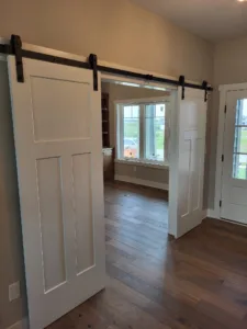 Painted white paneled barn door slid open on black overhead track, hallway visible beyond
