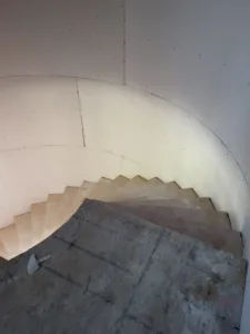 Curved staircase with unfinished treads and bare drywall walls, before any trim installed
