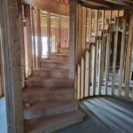 Rough framing and stair construction in progress with exposed studs, door openings, and unfinished stair treads.