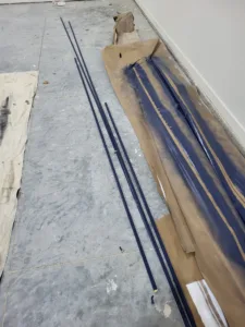 Dark painted rod stock and rails laid on paper on the floor before installation