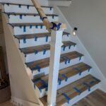 Staircase with finished wood treads, white risers, newel post, and handrail taped for paint protection.