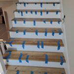 Finished wood stair treads and risers installed with painter's tape applied for protection before paint.