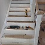 Wood stair treads installed over white-painted risers with newel post in progress.