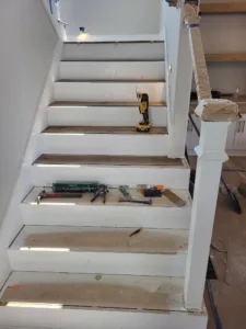 Wood stair treads installed over white-painted risers with newel post in progress.