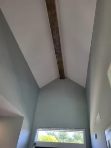 Wood beam running along the peak of a tall vaulted ceiling above a single window