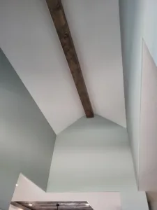 Dark stained wood beam running along a vaulted ceiling slope in a painted blue gray nook