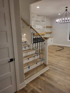 Iron baluster staircase with wood treads and handrail, tape applied to protect finish during staining.