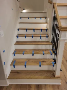 Interior staircase with taped wood treads, painted risers, and a black horizontal rod railing