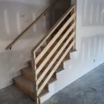 Horizontal rod railing installed on interior staircase with newel post and handrail, raw wood ready for finish.
