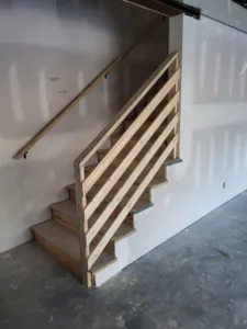 Interior staircase with a raw wood newel post and diagonal slat safety railing