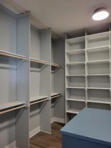 Painted white face frame closet shelving with vertical dividers and hanging rods, blue cabinet below.