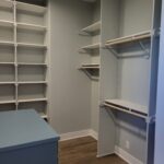 Completed walk-in closet with painted shelving, hanging rods, and built-in island countertop.