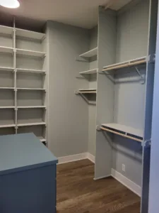 Walk-in closet with tiered painted shelves and hanging rods on both walls, blue island in foreground.