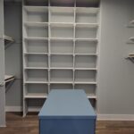 Custom built-in closet shelving system with grid-style white shelves and blue countertop island in walk-in closet.