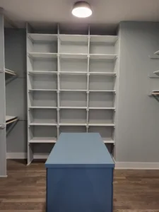 Walk-in closet with a grid of small white shelving compartments and a blue island dresser in center.