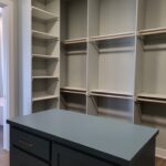 Finished walk-in closet with face-frame shelving, hanging rods, and painted island countertop with drawers.