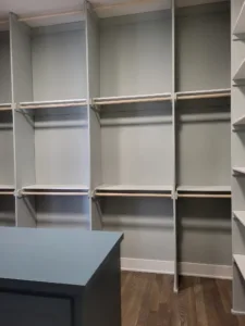 Walk-in closet with white painted shelving units, vertical dividers, and hanging rods installed.