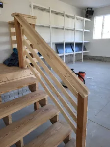Rough framed wood plank stair treads with a horizontal slat railing, unfinished stage