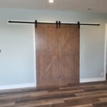 Finished barn doors with X-bracing hung on overhead track with black hardware and rollers installed.
