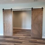 Two 6'8" barn door slabs with X-bracing hung on overhead track with black hardware; raw wood finish ready for stain or paint.