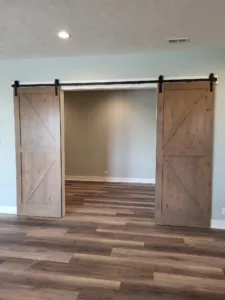 Unfinished raw wood barn door pair with X bracing hung open on black overhead track