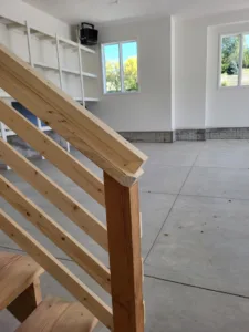 Horizontal wood slat railing installed on a staircase with a solid newel post, raw wood finish