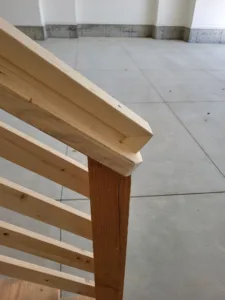 Unfinished wood horizontal slat railing with a mitered end cap where the top rail meets the post.