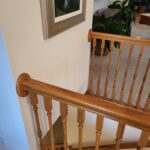 Completed wood baluster railing with turned spindles and stained handrail on residential staircase.
