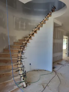 Curved staircase under construction with plywood treads and wall blocking, no railing installed yet