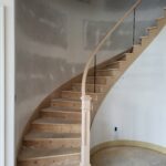 Curved staircase with finished newel post and glass baluster railing, raw wood treads ready for stain.