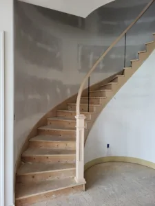 Curved interior staircase with raw wood treads and a newel post, ready for stain