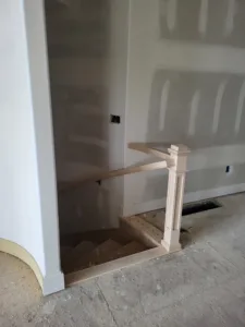 Unfinished wood newel post and curved handrail at a stairway opening during drywall stage
